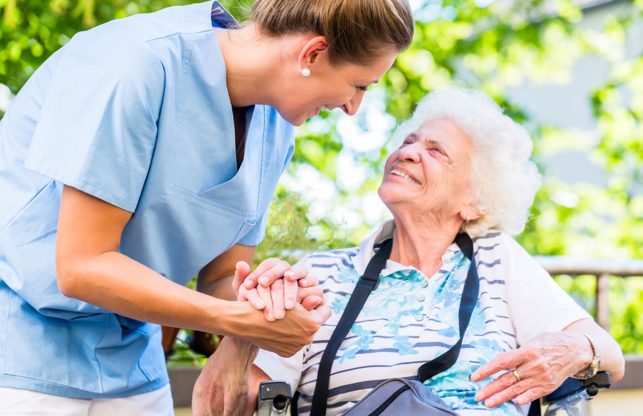 Eine Pflegekraft hält die Hand einer Seniorin, was Zuneigung und Mitgefühl ausdrückt.